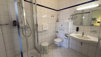 Een badkamer met een glazen douchecabine, toilet, wastafel en spiegel.