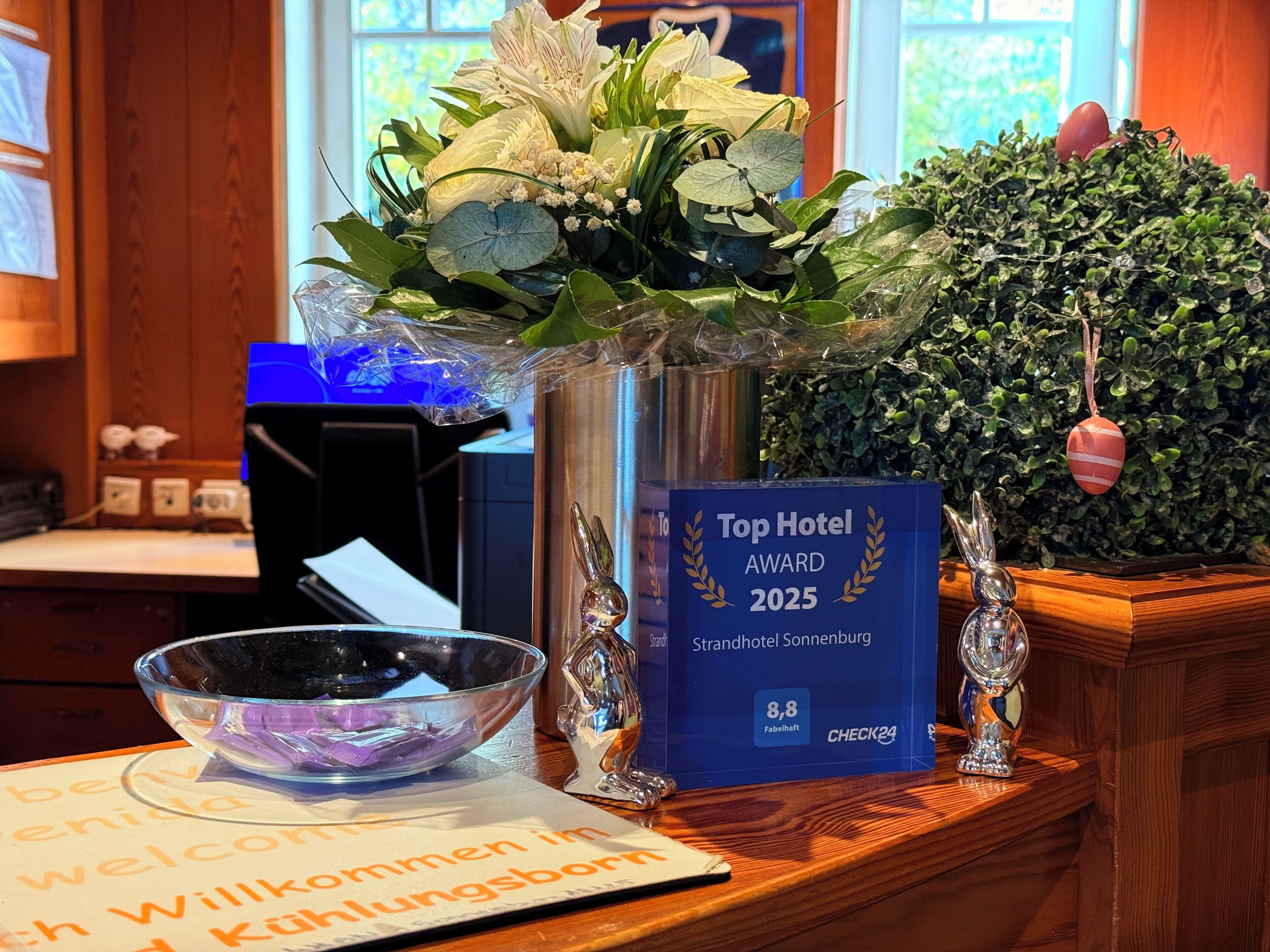 A reception desk with a vase of flowers, a framed award for 'Top Hotel Award 2025', and a decorative bunny figurine.