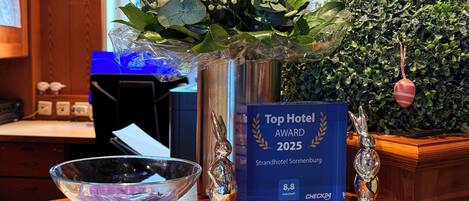 Un mostrador de recepción con un jarrón de flores, un premio enmarcado por 'Top Hotel Award 2025' y una figurita de conejo decorativa.