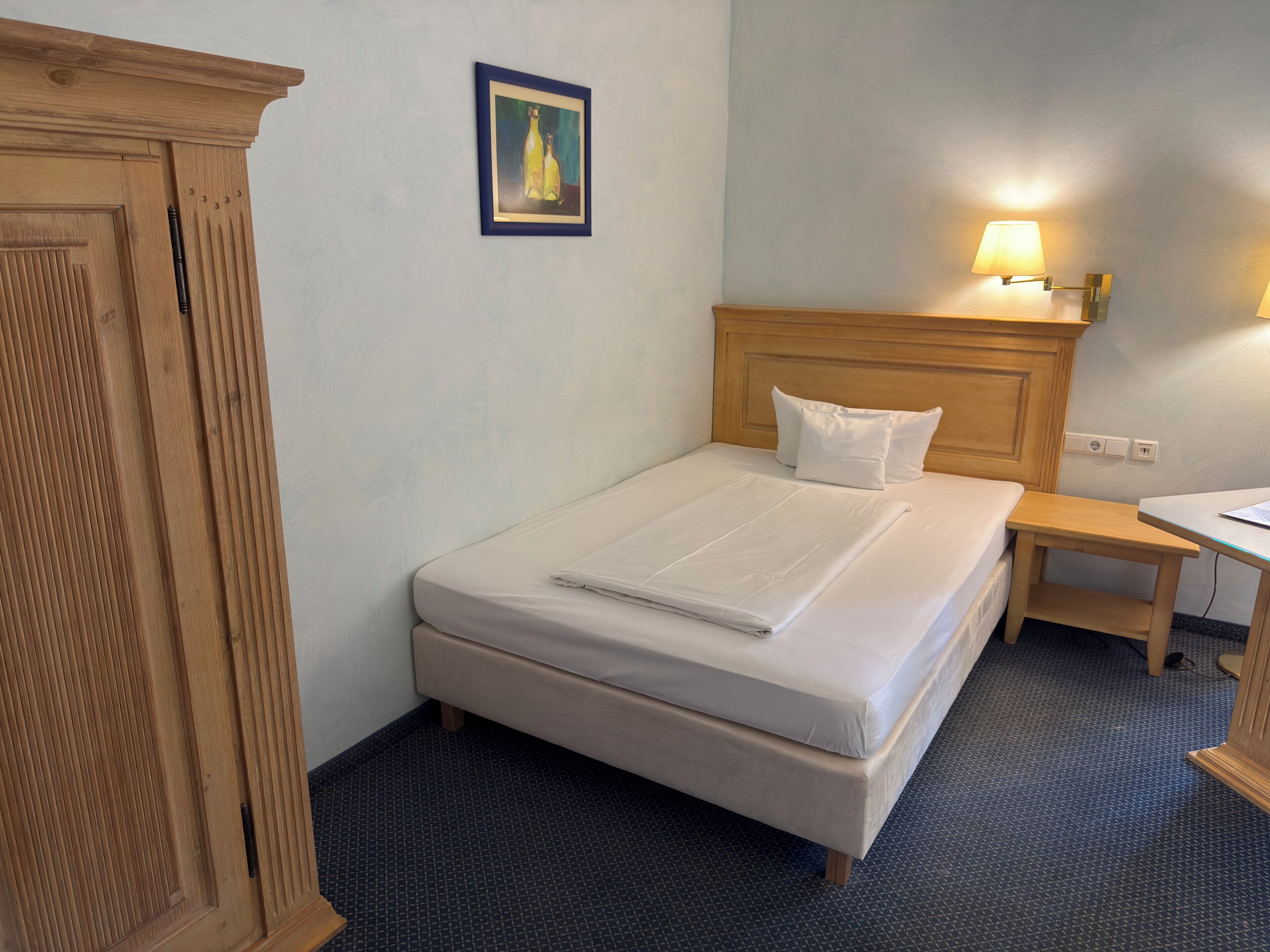 A hotel room with a bed, bedside table, lamp, and a wooden wardrobe.