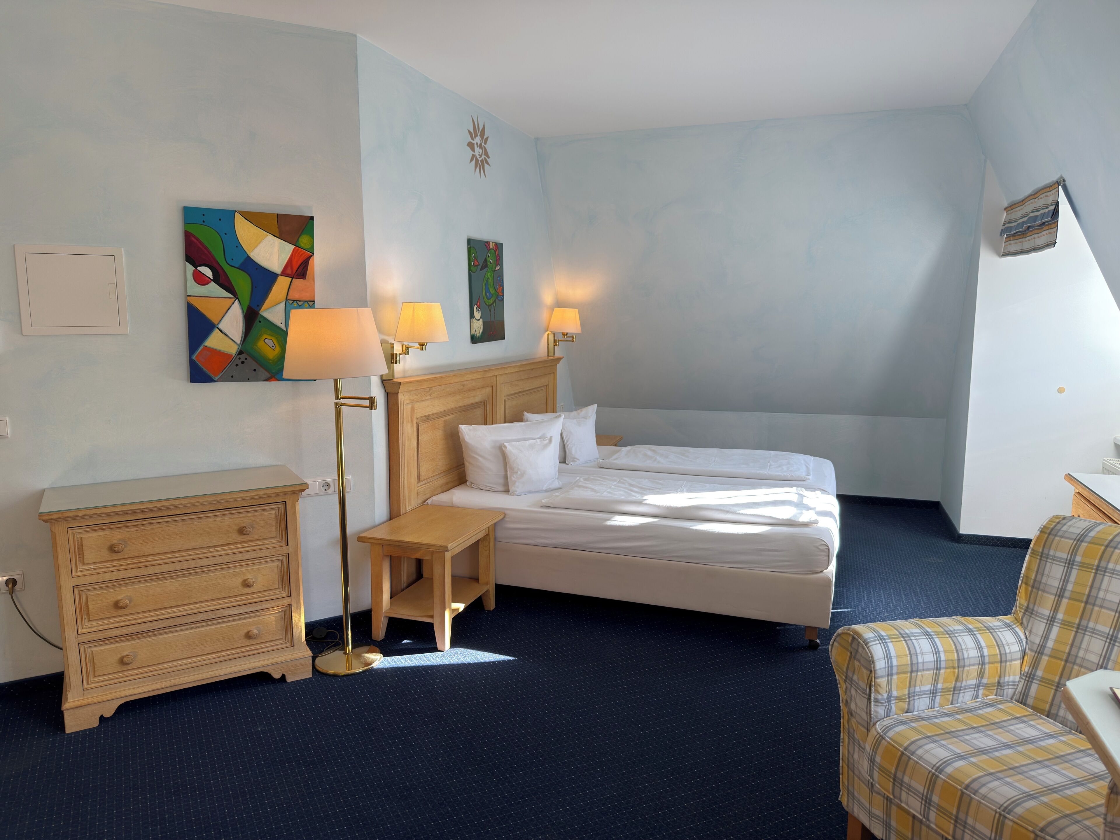 A hotel room with a bed, bedside tables, a chair, and artwork on the walls.