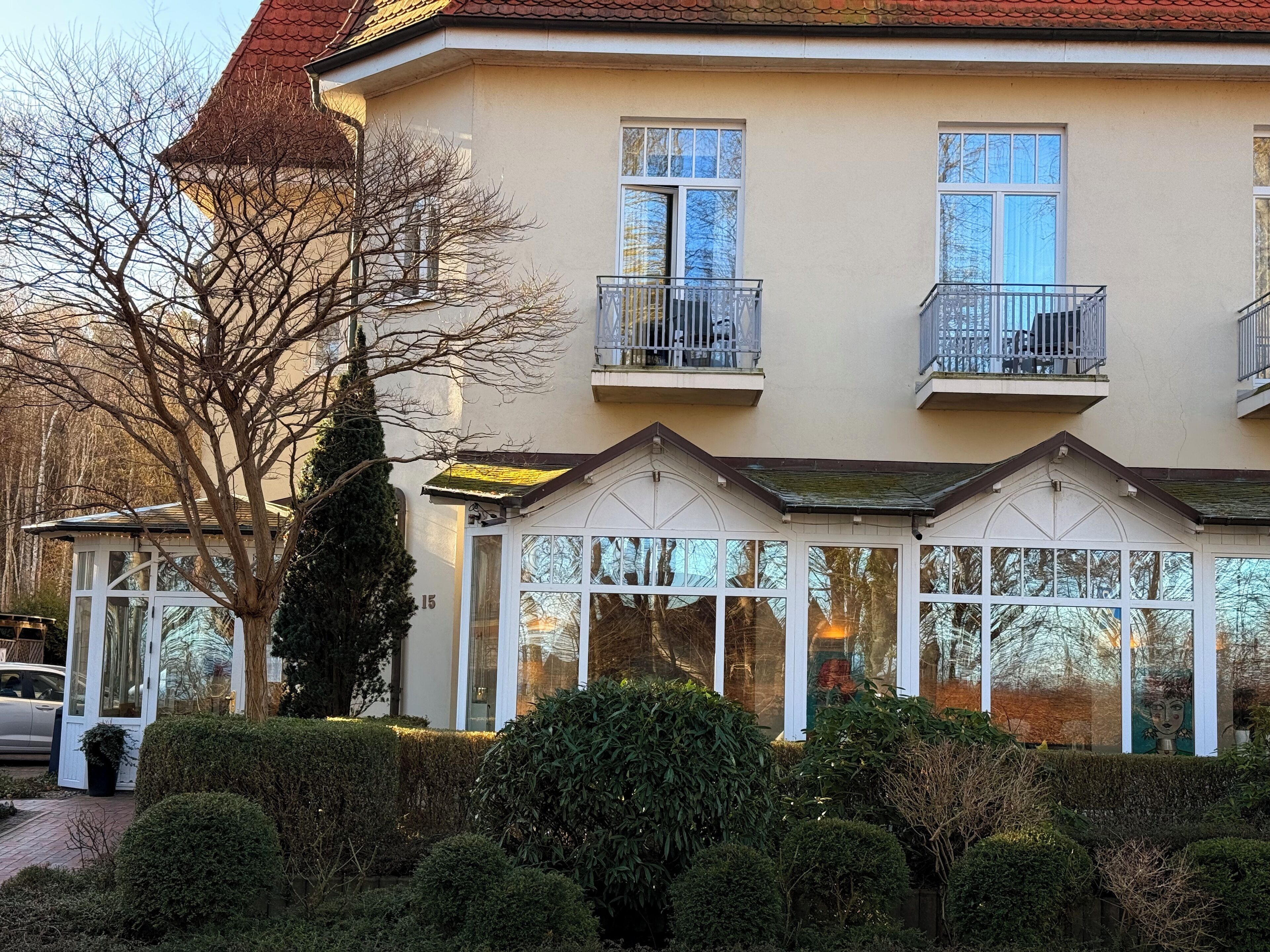 A two-story building with a balcony, a conservatory with glass doors, and a number '15' on the facade.