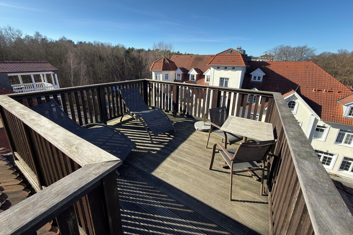 A wooden deck with outdoor furniture, a view of houses with red roofs, and a clear sky.