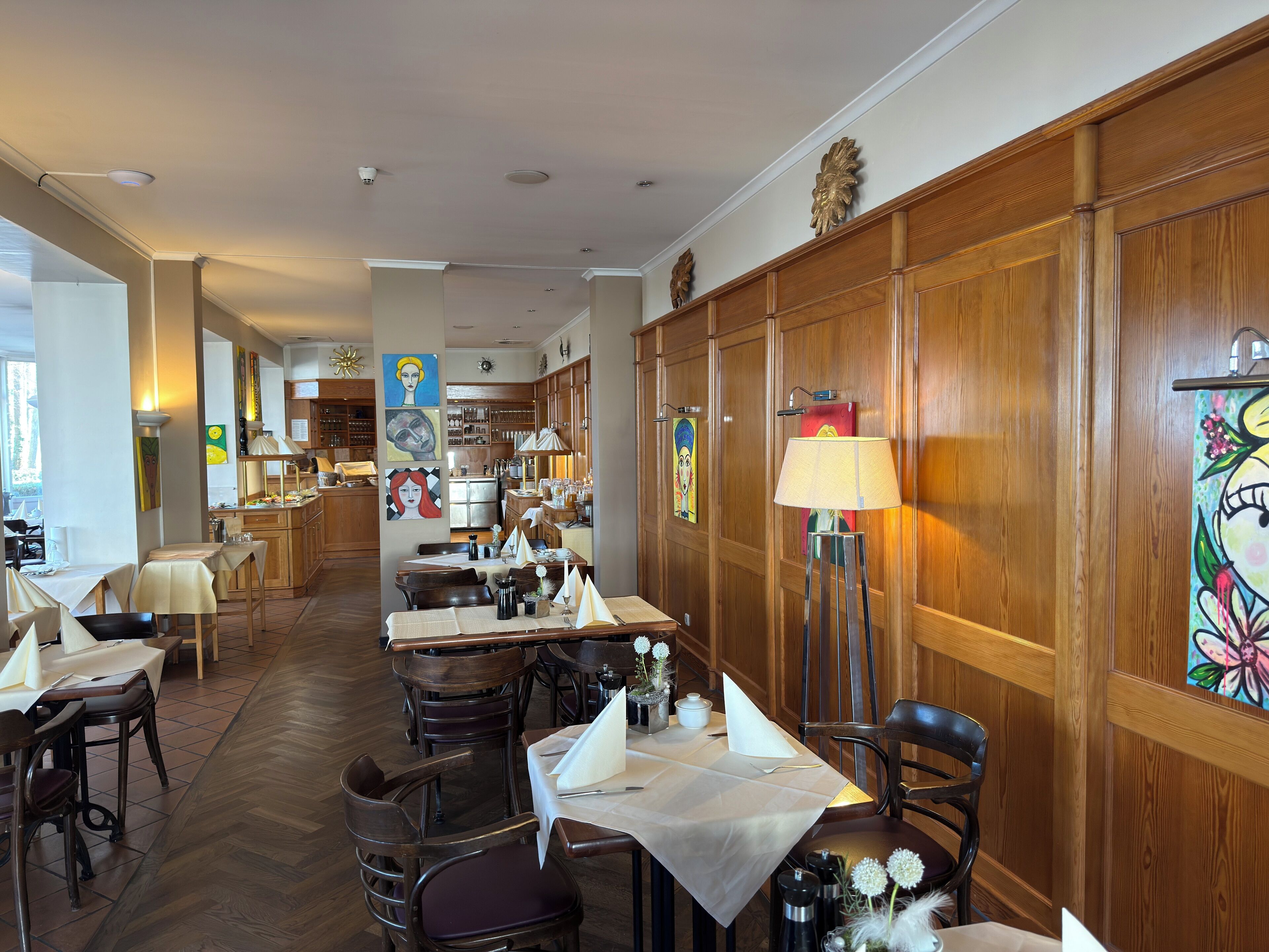 A restaurant with wooden paneling, tables with white tablecloths, and artwork on the walls.