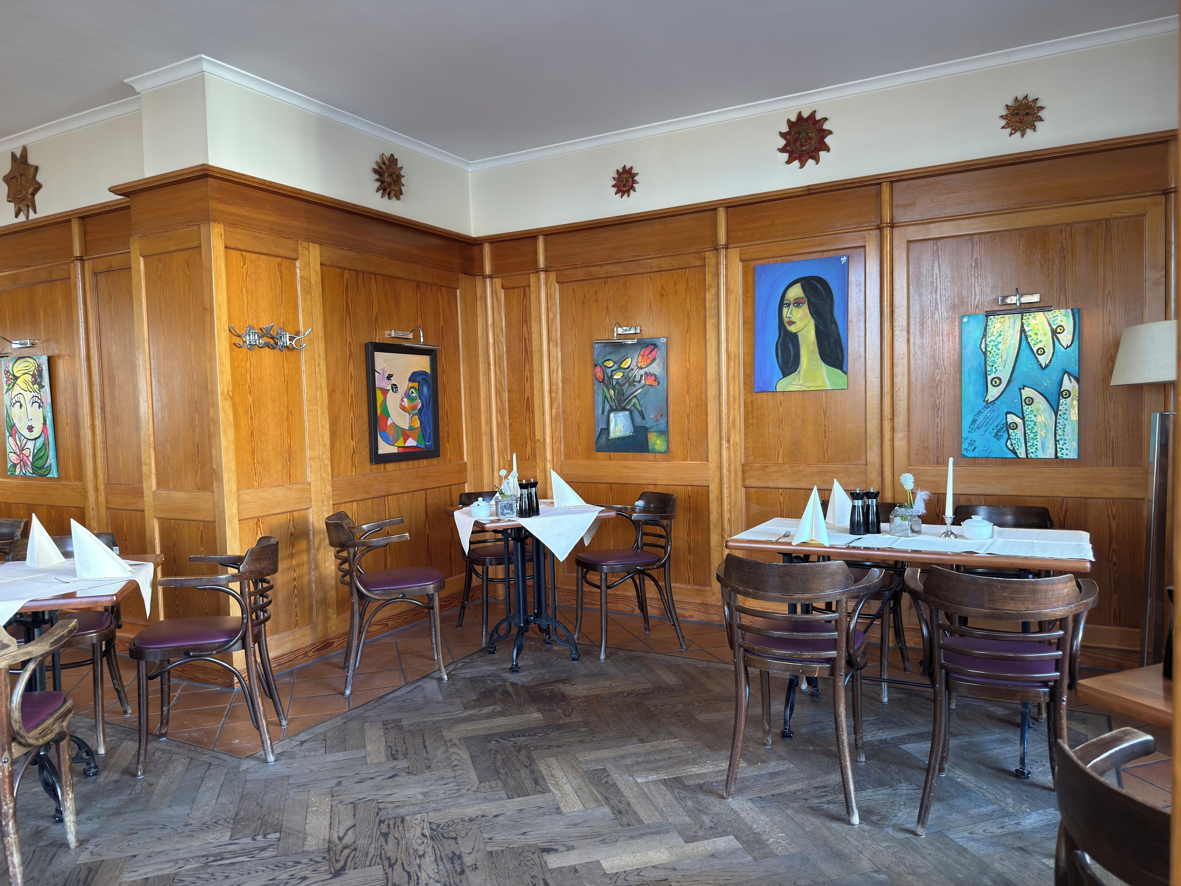 Un comedor con paneles de madera, varias mesas y sillas, y obras de arte en las paredes.