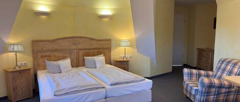 A hotel room with a double bed, two bedside tables with lamps, a plaid armchair, and a small wooden dresser.
