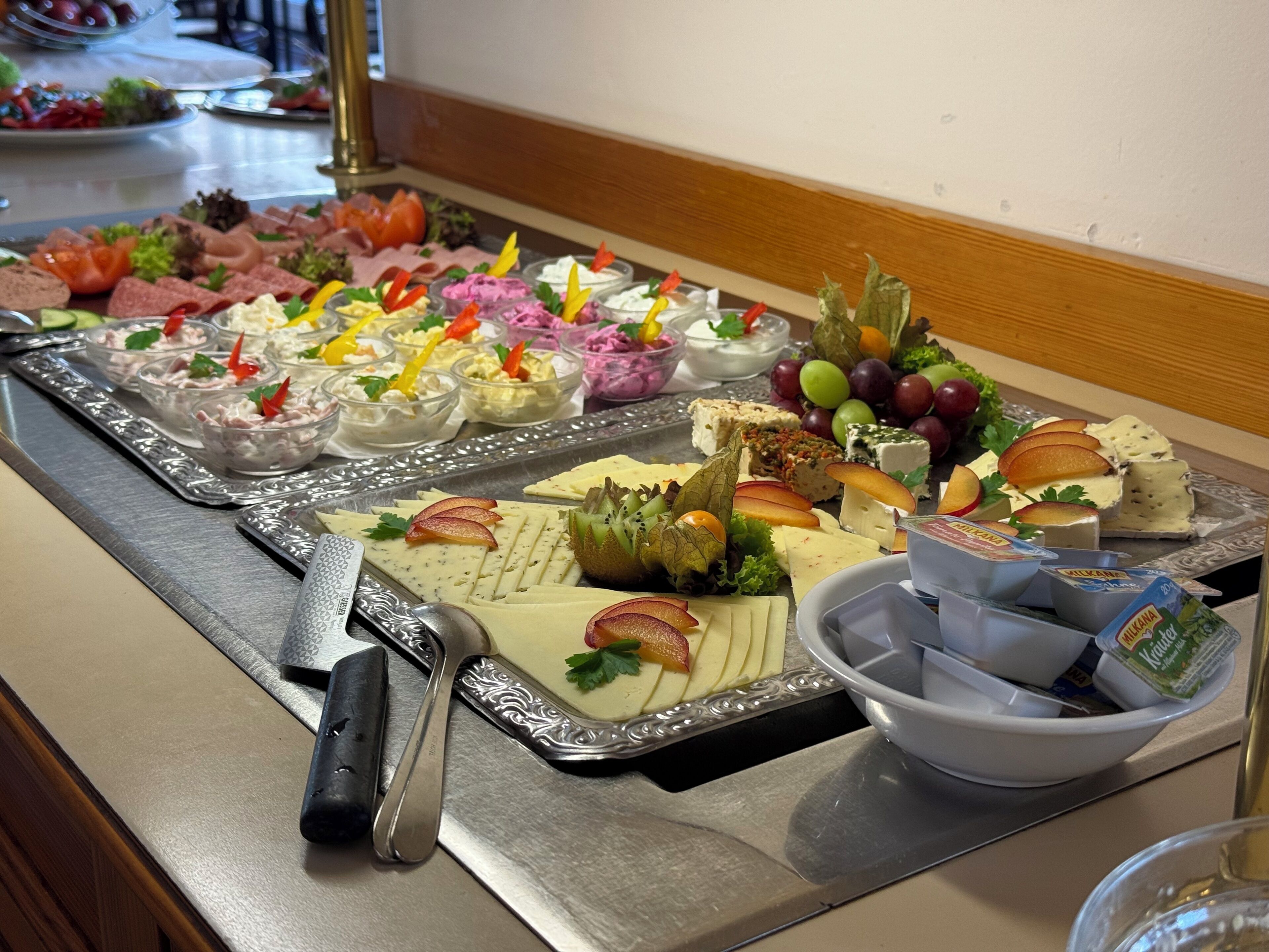 A buffet with various food items, including cheeses, fruits, and dips, arranged on trays.