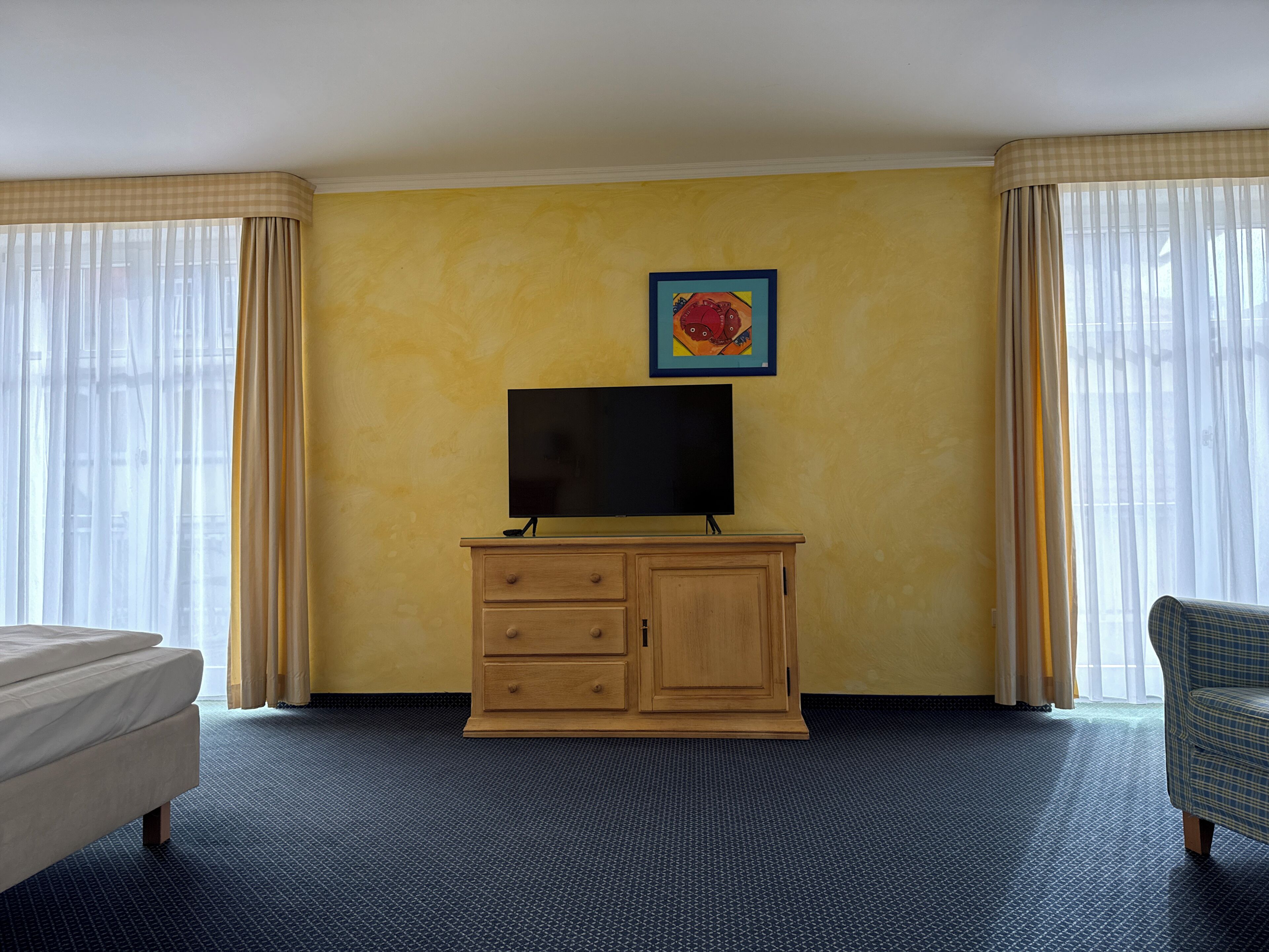 A hotel room with a bed, a television on a wooden cabinet, a painting on the wall, and a chair.