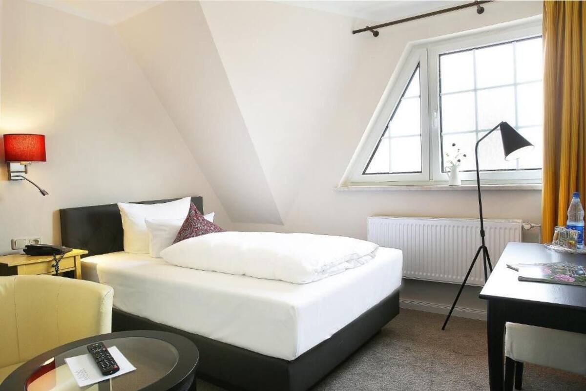 Hotellihuone, jossa on sänky, työpöytä, tuoli, lamppu, ikkuna ja patteri.