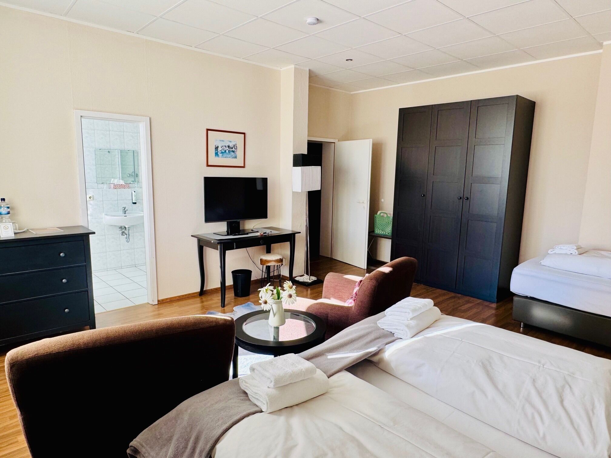 Ett hotellrum med en säng, ett skrivbord med en dator, en stol, en garderob och ett badrum.