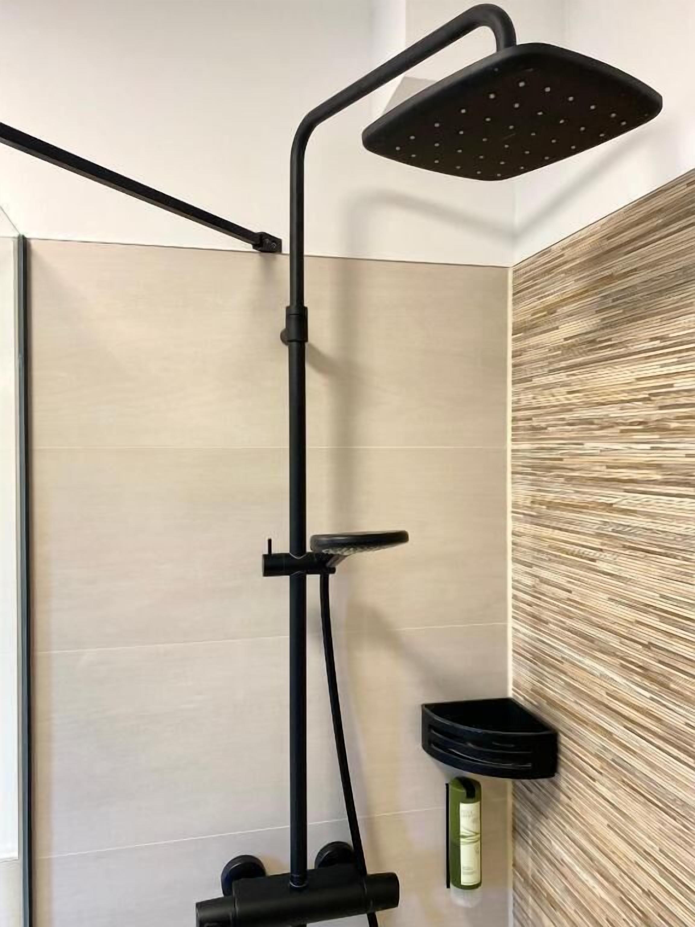 A modern shower with a black frame, a handheld showerhead, and a bottle of shampoo.