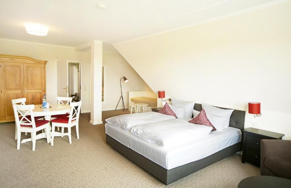 A bedroom with a bed, bedside tables, a desk with chairs, and a wardrobe.