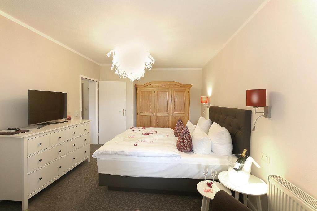 Une chambre d’hôtel avec un lit, une télévision, une commode, une table de chevet avec une bouteille et une lampe.