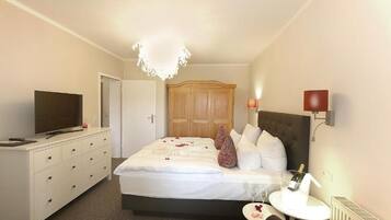 Une chambre d’hôtel avec un lit, une télévision, une commode, une table de chevet avec une bouteille et une lampe.