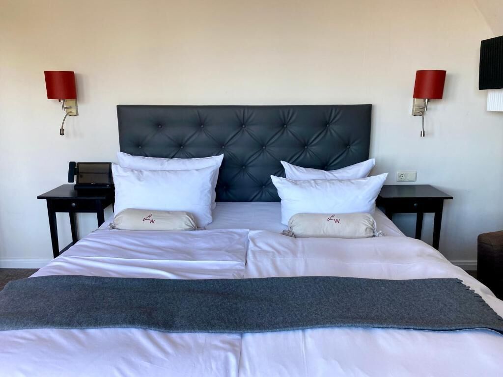 A neatly made bed with a tufted headboard, two bedside tables, and red wall sconces.