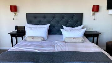A neatly made bed with a tufted headboard, two bedside tables, and red wall sconces.