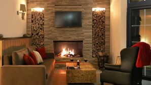 A living room with a fireplace, a television mounted above it, and a sofa with red cushions. - Hotel Wittenbeck by ANS (Wittenbeck)
