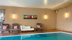 A swimming pool with lounge chairs and a sofa, a painting on the wall, and a light fixture. - Hotel Wittenbeck by ANS (Wittenbeck)