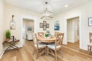 A dining area with a round wooden table, four chairs, and a hanging light fixture. - Mid-Tide Modern - Easy Walk, Easy Stay, Easy Living (Galveston)