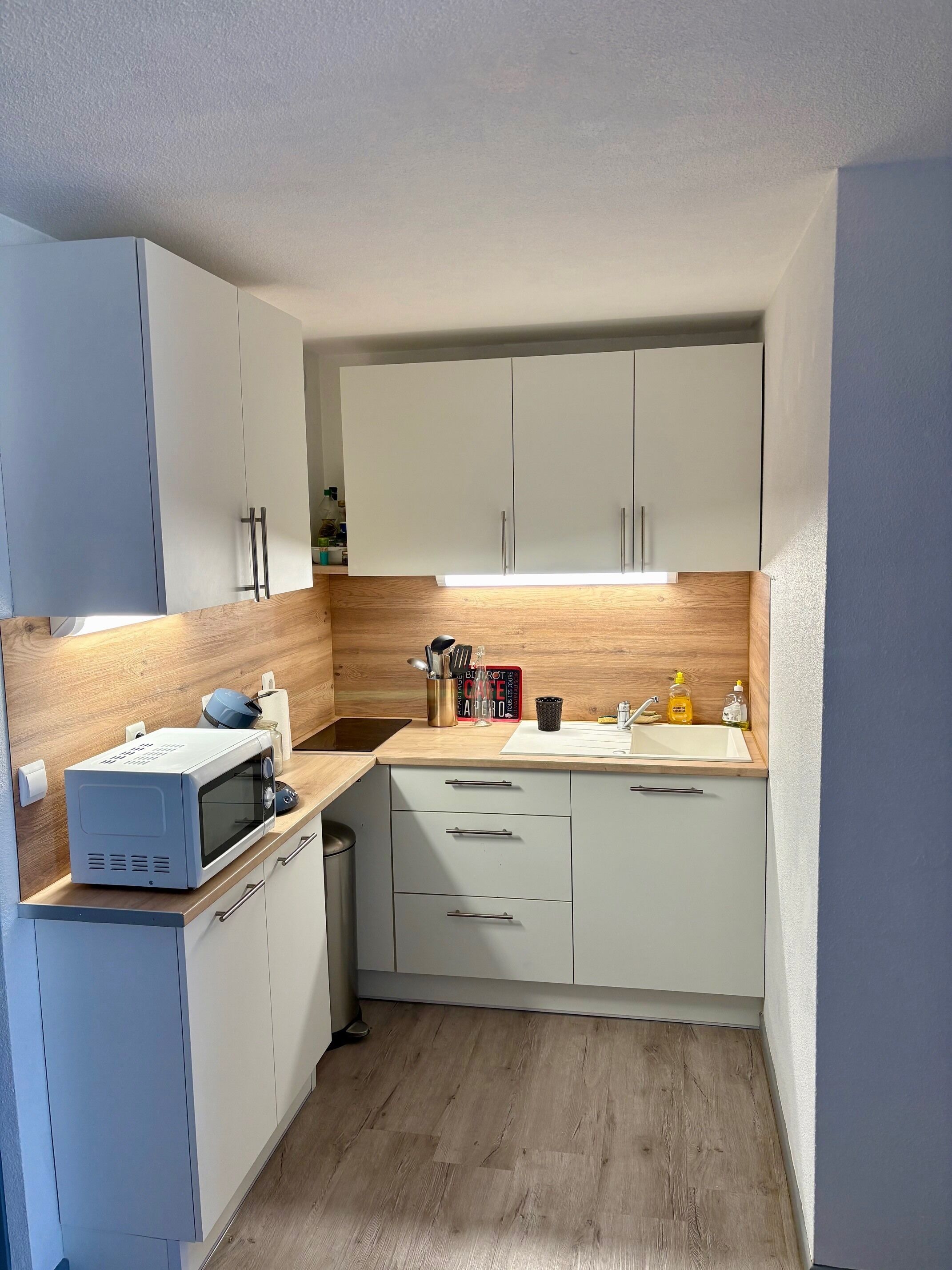 Cocina compacta con armarios blancos, microondas, pileta y encimeras de madera.