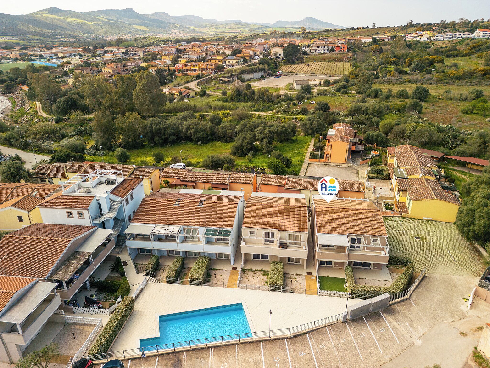 A residential area with terraced houses, a swimming pool, and a view of the surrounding landscape.