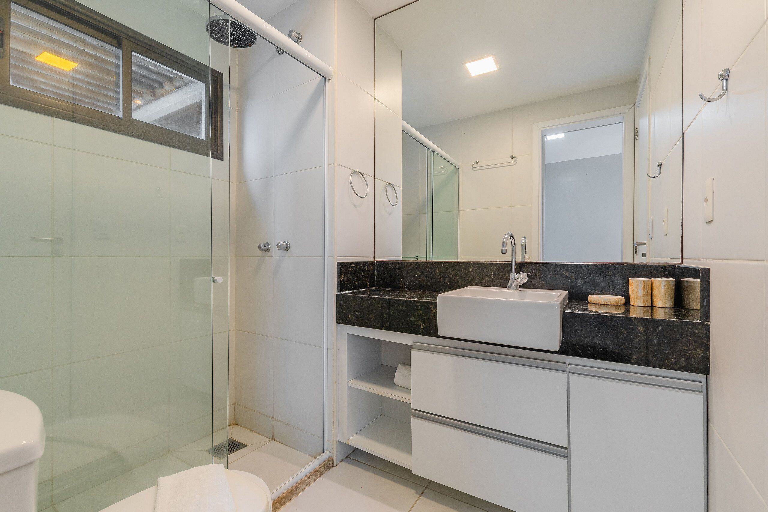 Een moderne badkamer met een douchecabine van glas, een witte wastafel en een grote spiegel.