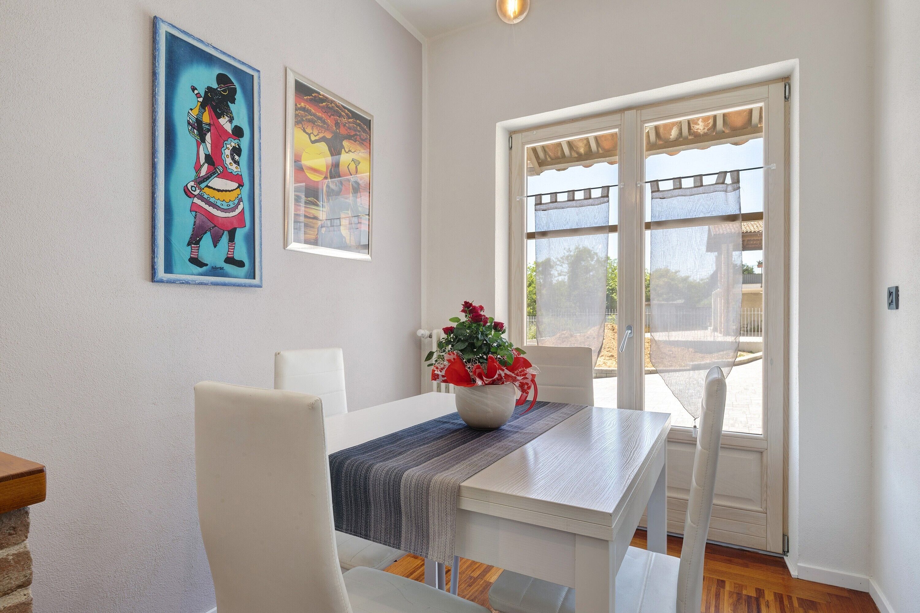 A dining area with a table, chairs, a vase with flowers, and artwork on the wall.