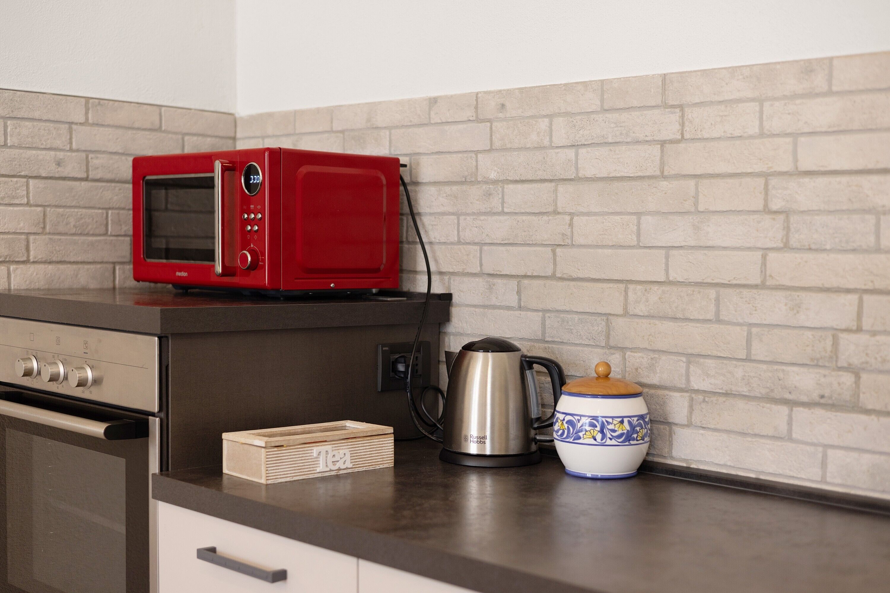 A kitchen with a red microwave, a kettle, a tea box, and a decorative bowl on the counter.