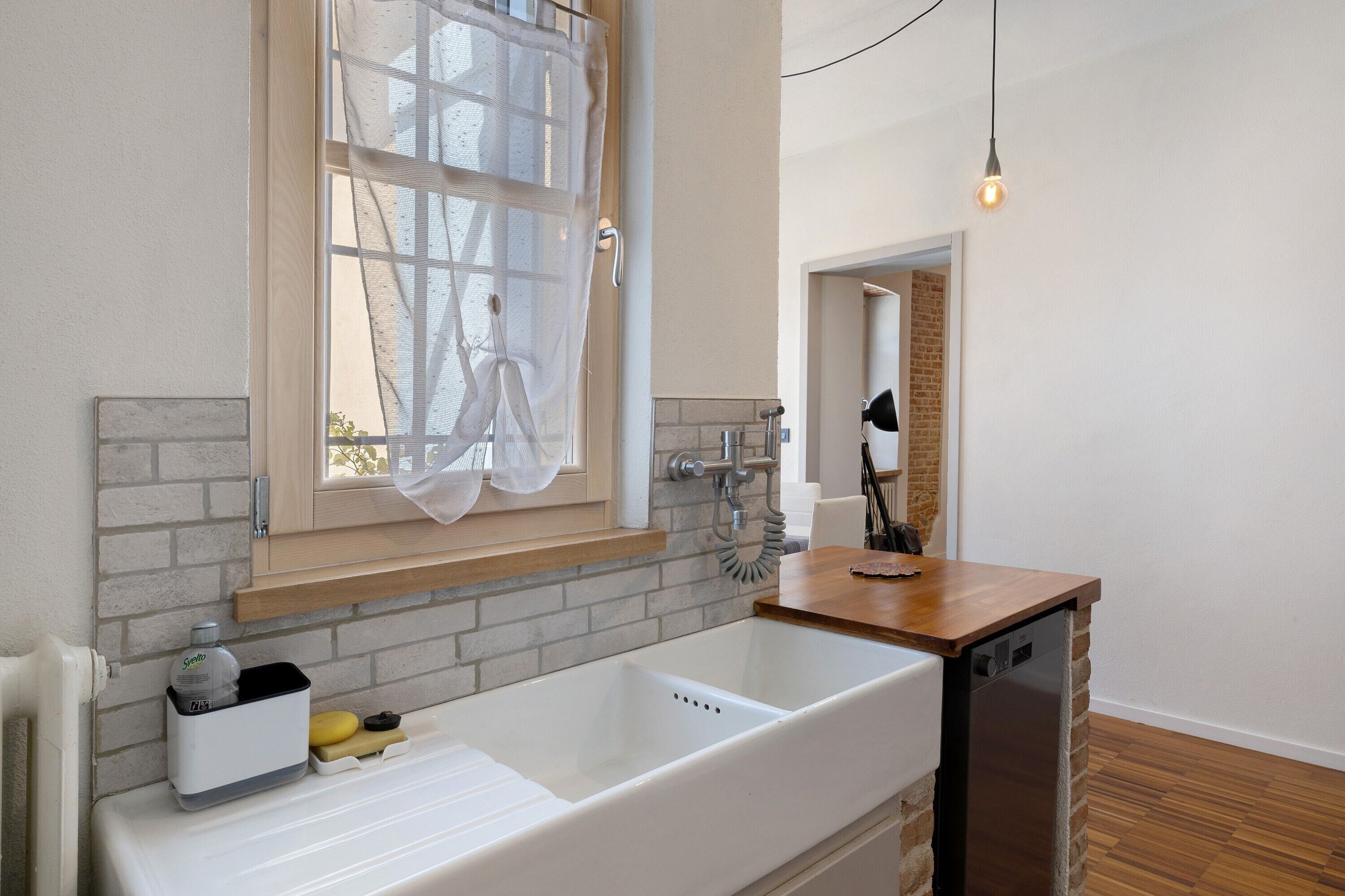 Ein modernes Badezimmer mit einem großen weißen Waschbecken, einer Holz-Arbeitsplatte, einem Handtuchhalter und einem Fenster mit leichtem Vorhang.