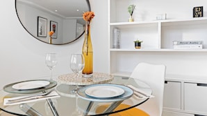 Een moderne eetruimte met een glazen tafel, witte stoelen en een ronde spiegel erboven.