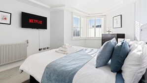 Een moderne slaapkamer met een groot bed, een flatscreen televisie aan de wand, een radiator en een raam met zonwering.