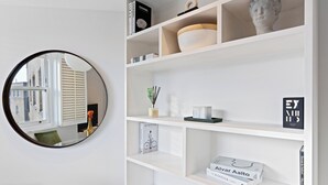Een modern interieur met een witte boekenkast, een ronde spiegel en uitzicht naar buiten.