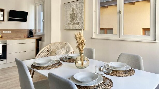 A dining area with a white table set for four, a woven placemat, and a vase with dried plants. - Quiet apartment near train station and Quimper historic center (Quimper)