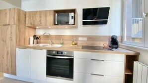 A modern kitchen with wooden cabinets, a built-in microwave, a dishwasher, and a window providing natural light. - Quiet apartment near train station and Quimper historic center (Quimper)