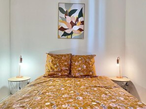 A bedroom with a floral bedspread, two bedside lamps, and a wall-mounted abstract painting.