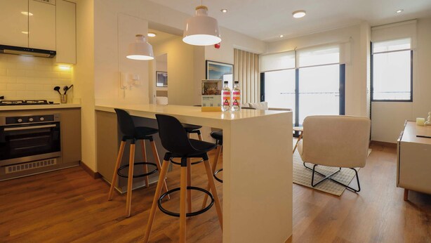 Una cucina moderna con isola centrale, sgabelli da bar e zona pranzo con una sedia.