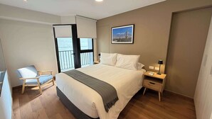 Una camera da letto con un letto, una sedia, un comodino, una lampada, un quadro appeso al muro e una porta che dà su un balcone.