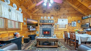 A cozy log cabin interior with a fireplace, wooden walls, a dining area, and a television. - Cozy Cabin Near TOWN! Hot Tub | Fire Pit | Arcade (Sevierville)