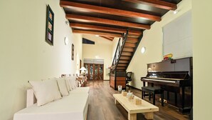 Un amplio salón con un sofá, una mesa de centro de madera, un piano y una escalera.