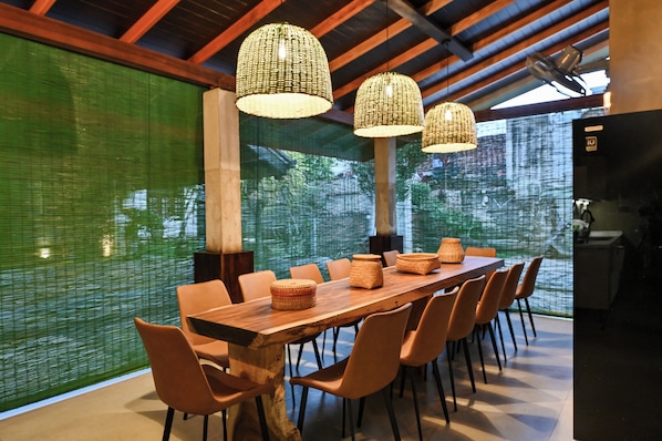 A modern dining area with a long wooden table, orange chairs, and three woven pendant lights.