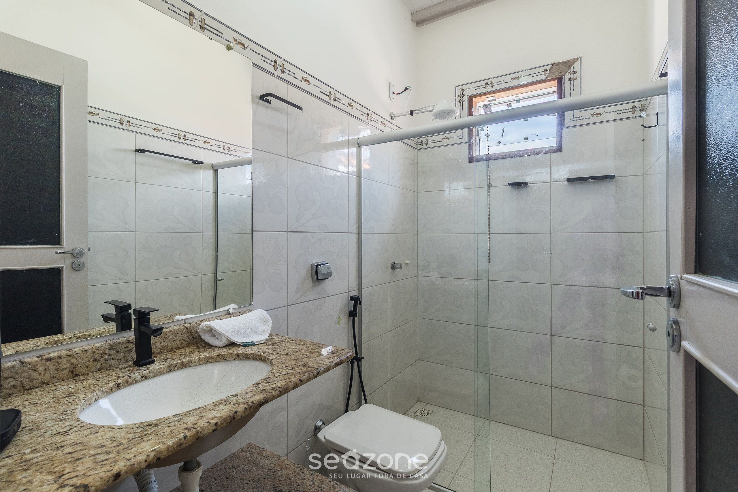 A bathroom with a granite countertop sink, a toilet, and a glass shower enclosure.
