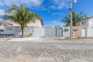 A paved courtyard with cobblestone flooring, a palm tree, and a gated entrance to a building. - Condo w/ Pool and BBQ Grill - ART (Porto Seguro)