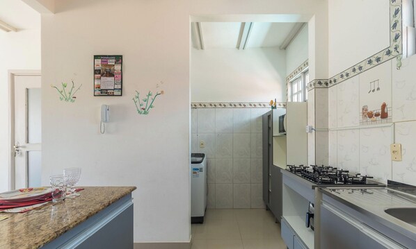 Une cuisine équipée d’un plan de travail, d’une cuisinière et d’un réfrigérateur. Une porte donne accès à une autre pièce.