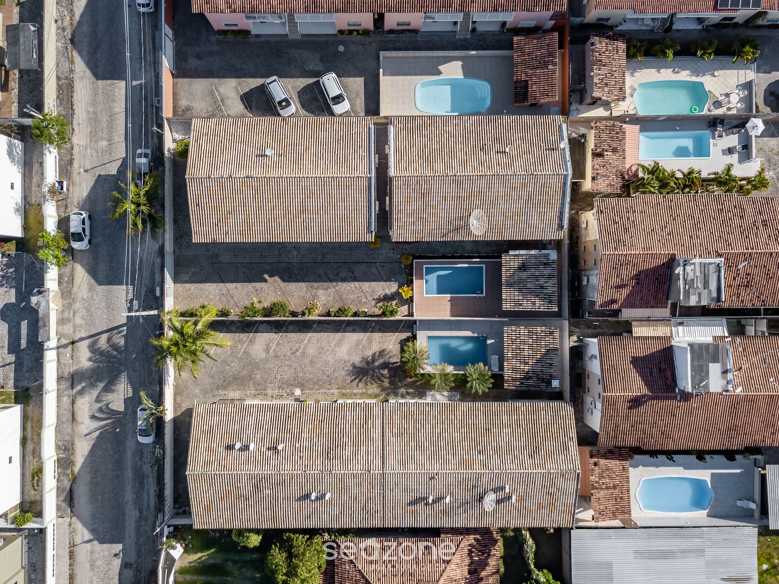 An aerial view of a residential area with multiple houses, each featuring a tiled roof and a swimming pool.