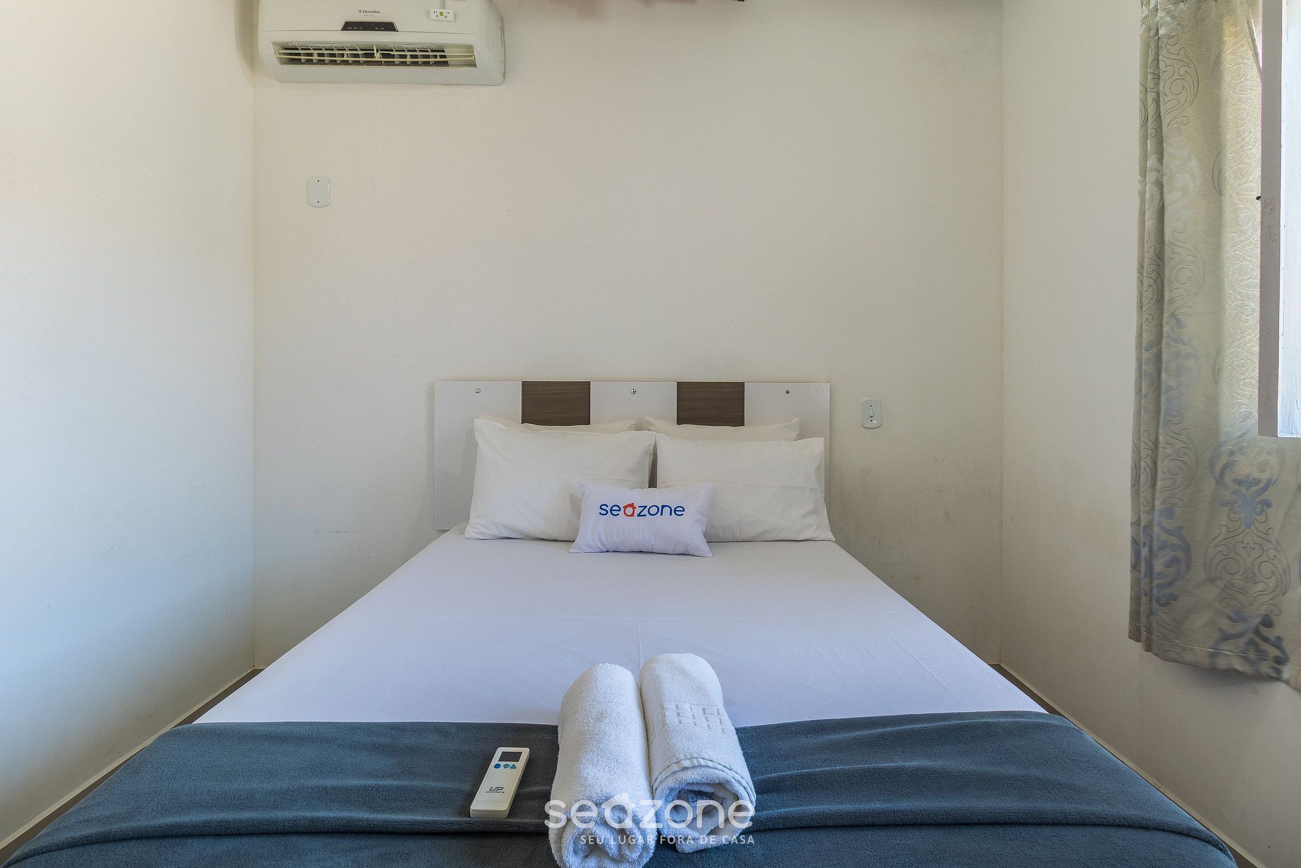 A single bed with a white headboard, a pillow with "seozone" branding, and a remote control on the bed.