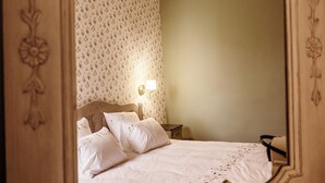 A bedroom with a large mirror, a bed with white linens, a nightstand with a lamp, and a wooden dresser. - Château de la Grange Moreau - Chambre Claude de Dommaigné (Vallon-sur-Gée)