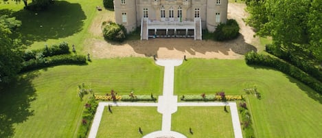 An aerial view of a large, historic building with a symmetrical garden layout, including a central fountain and manicured lawns.