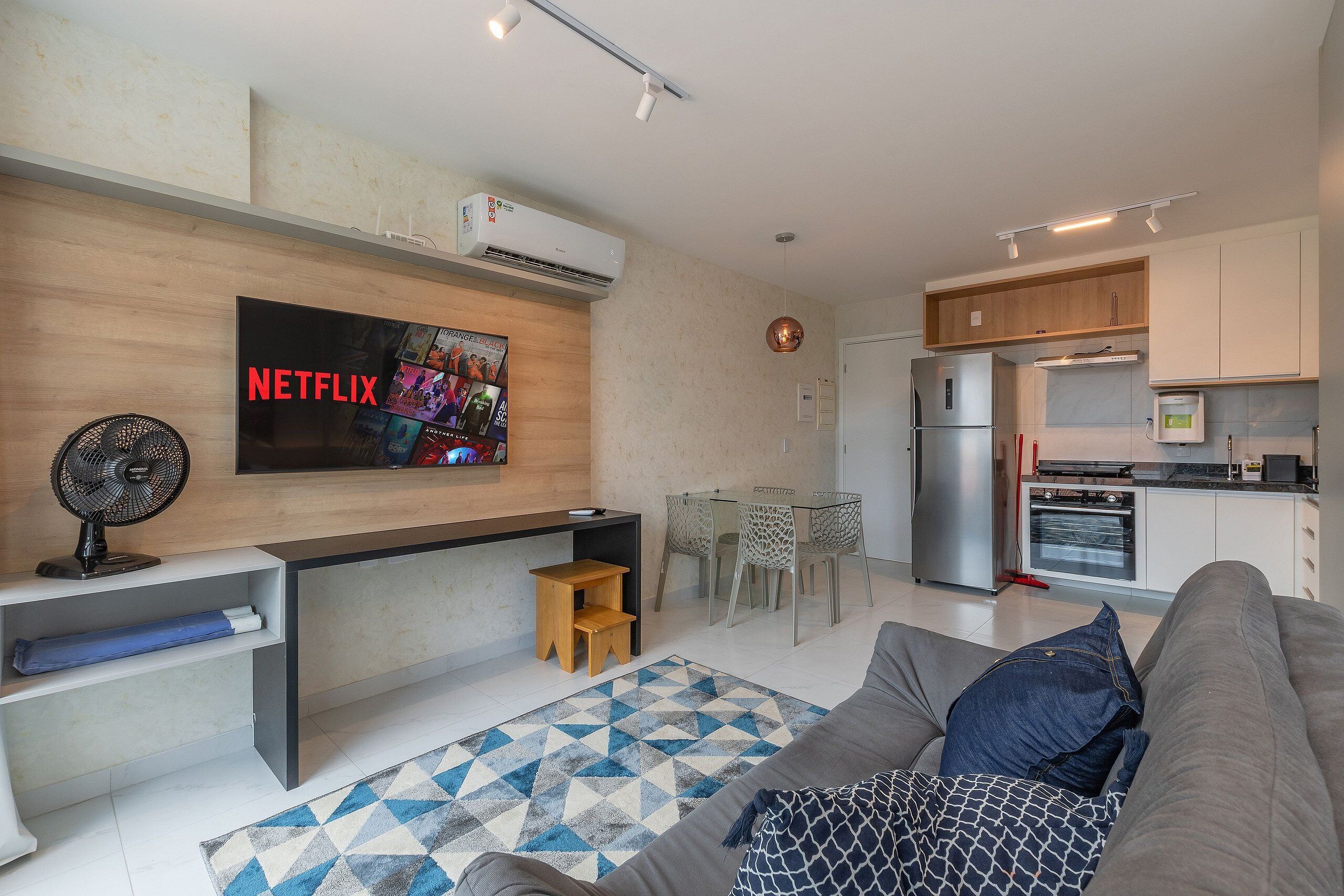 Una sala de estar moderna con un sofá gris, una mesa de centro y un televisor en la pared mostrando el logotipo de Netflix.