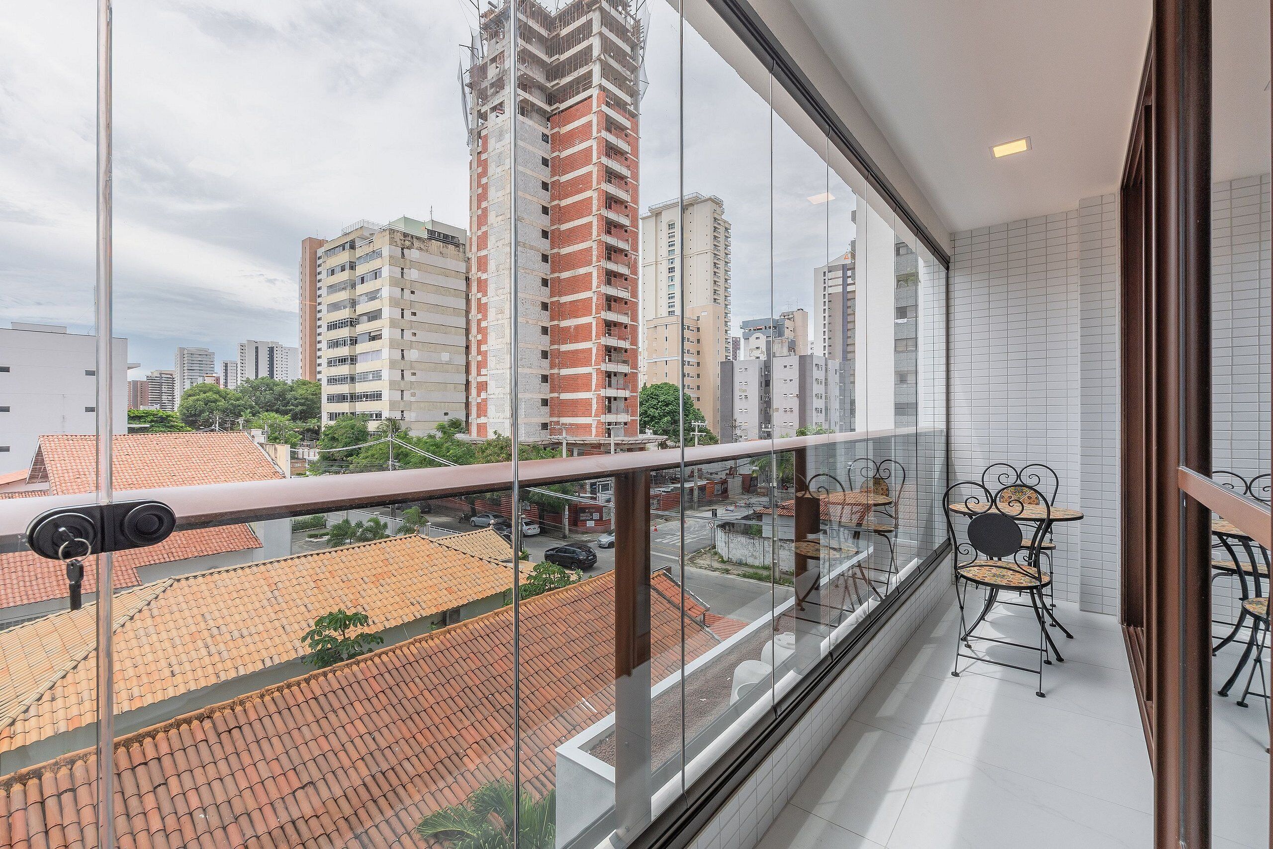 Un balcón con vista a la ciudad, sillas de metal y suelo de baldosas.