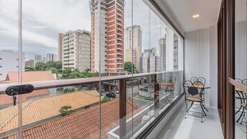 Un balcón con vista a la ciudad, sillas de metal y suelo de baldosas.